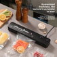 Black vacuum sealer on a kitchen counter beside vacuum sealed bags of corn, salmon and meat