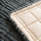 Corner of a dark gray plush sofa cover lifted to show the cream quilted dotted backing