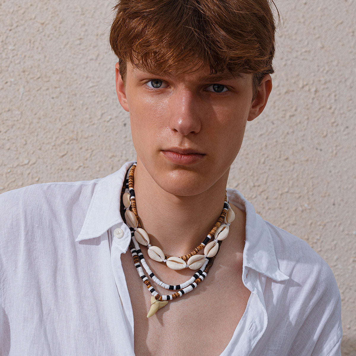 Close view of the layered shell necklace set worn open collar, cowrie row above the tooth pendant