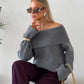 Grey off-shoulder fold-over knit sweater with wide cuffs worn with burgundy trousers