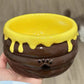 Hand holding a brown ceramic honey jar bowl with yellow drips and a paw print, close view