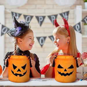 Two children in Halloween costumes holding lit orange pumpkin party bags at a decorated table