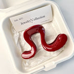 Large wine red wavy acrylic hair claw clip resting in a cream gift box with brand card