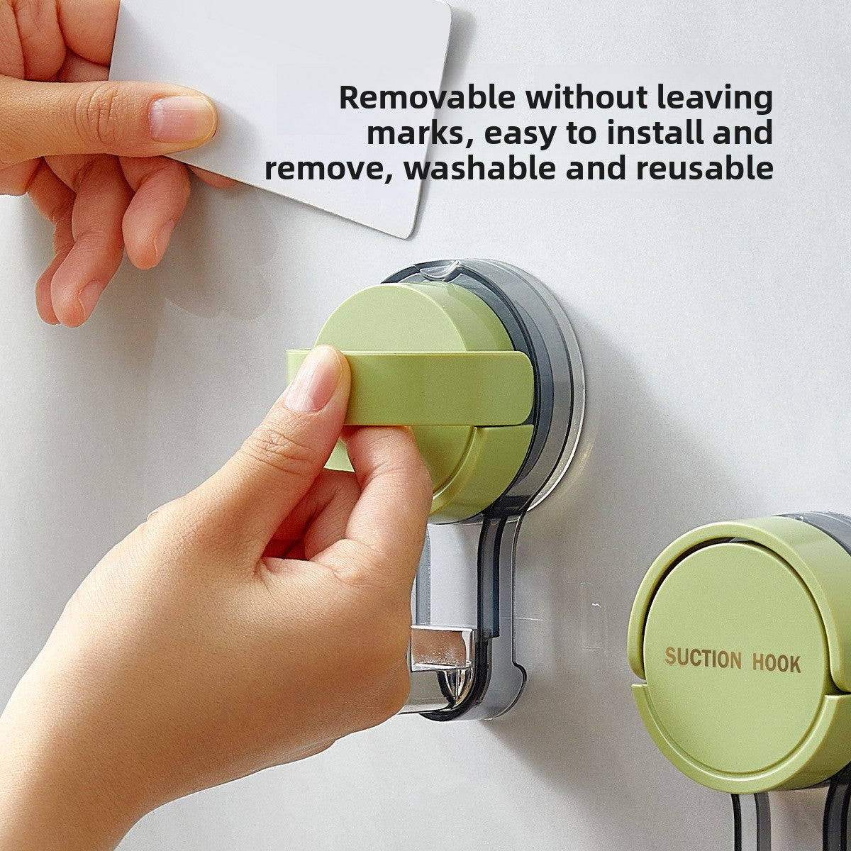 Hand pressing the lever cap of a green suction cup hook on a white wall beside a second hook