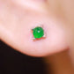Two dainty green stone stud earrings with four prong claws resting across two fingers