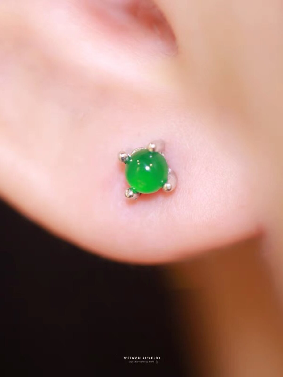 Two dainty green stone stud earrings with four prong claws resting across two fingers