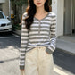 Gray and white striped long sleeve henley top with ribbed cuffs worn with cream jeans, hand in pocket