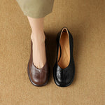 Brown and black embossed leather block heel slip-on shoes on a woven carpet beside a woman's foot