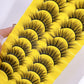 Thick fluffy cat eye false strip eyelashes in black on a yellow ten pair tray, angled view of the black strip lashes