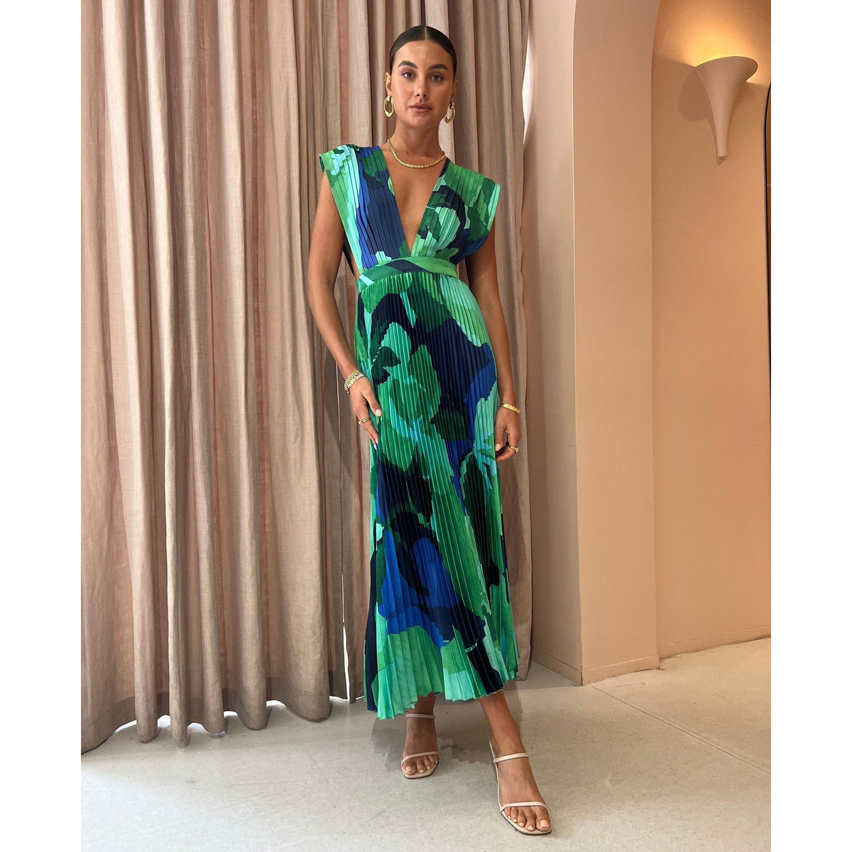 Model wearing the green abstract pleated maxi dress in a lit corridor