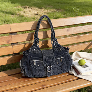 Blue washed denim shoulder bag with buckle flap resting on a park bench