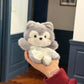 Grey plush husky squishy bean bag toy in one hand, brushed faux fur and dotted cotton apron