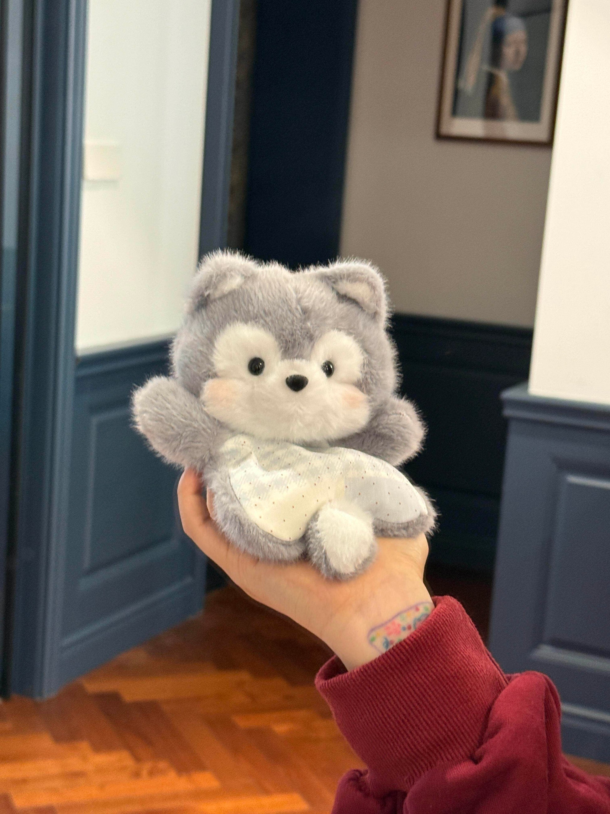 Grey plush husky squishy bean bag toy in one hand, brushed faux fur and dotted cotton apron