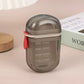 Closed smoke gray travel soap case with a red tab standing beside a wooden coaster and a book