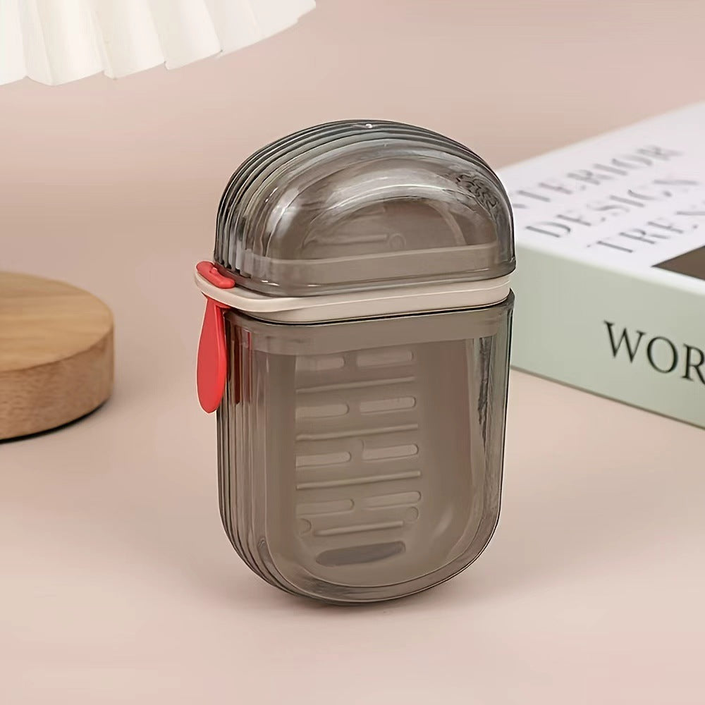 Closed smoke gray travel soap case with a red tab standing beside a wooden coaster and a book