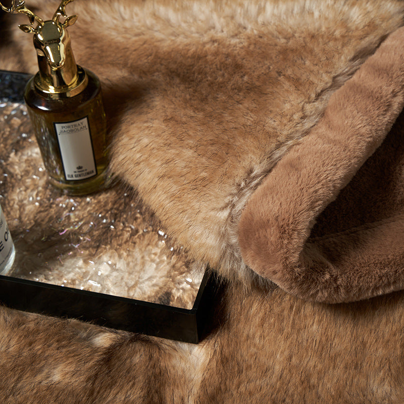 Close-up of the long camel fur pile and the stitched border of the blanket, with a perfume bottle