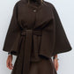 Khaki belted cape jacket with a stand collar and wide cape cut sleeves worn over trousers