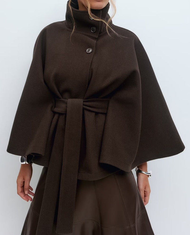 Khaki belted cape jacket with a stand collar and wide cape cut sleeves worn over trousers