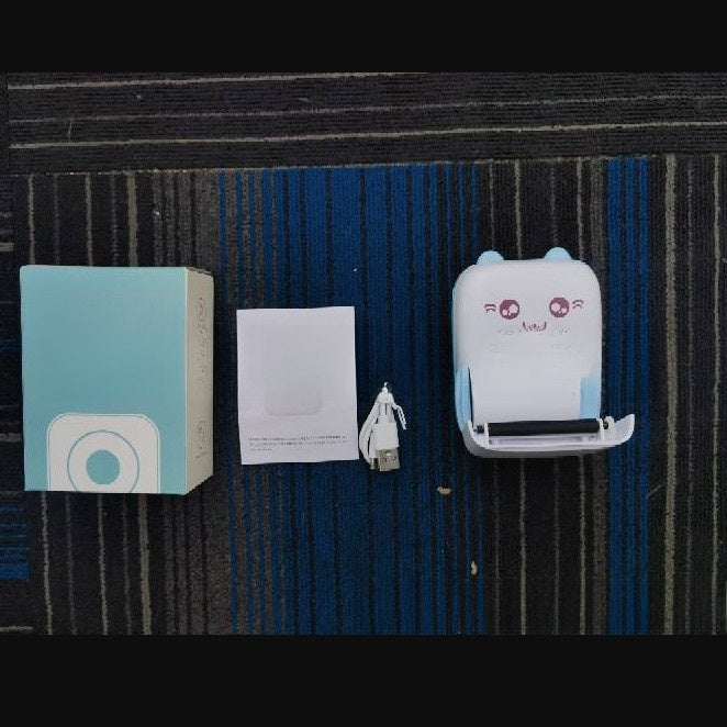 Top view of a box, paper roll, cable and a teal cat ear thermal printer on a dark mat, C9 blue option