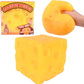 Yellow squeeze cheese block toy beside its retail box, with a hand pressing a rounded cheese toy