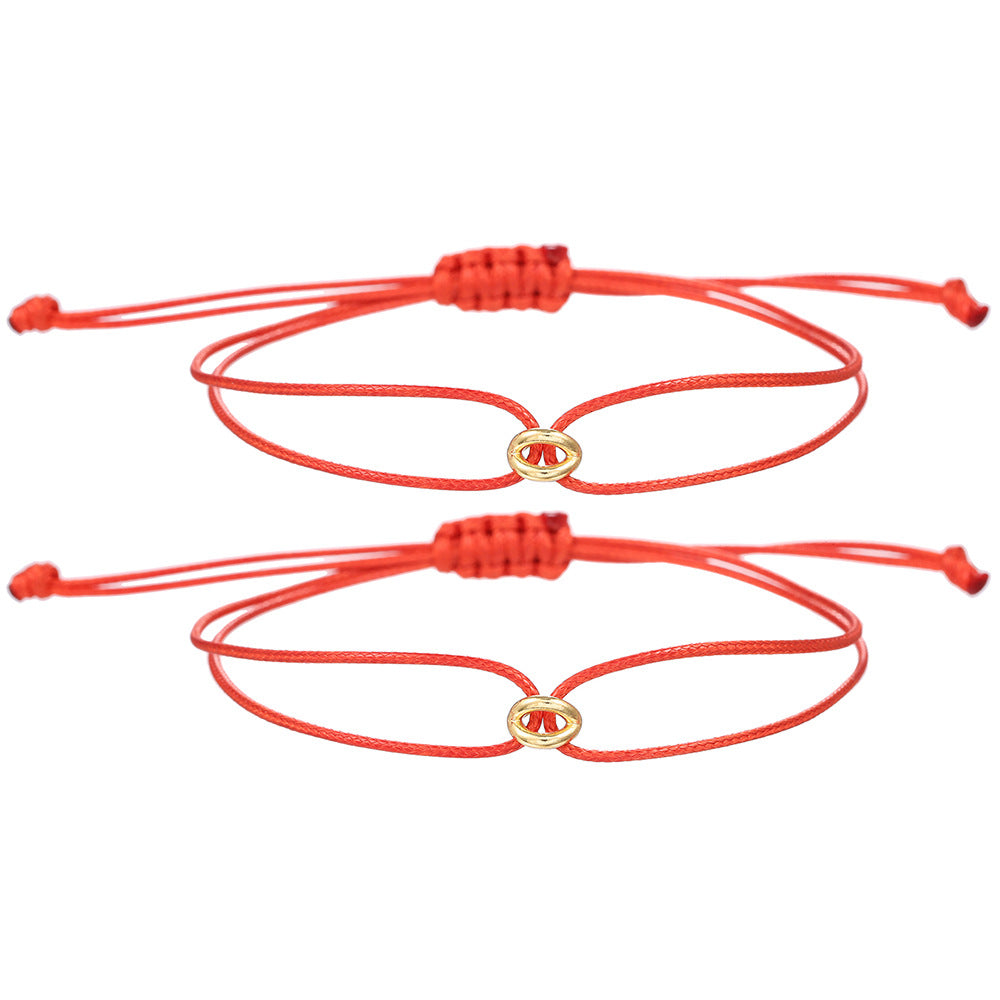 Two red cord bracelets with small gold tone charms and slide knots laid flat