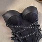 Angled view of the black bustier corset top showing molded cups and studded elastic crossover straps