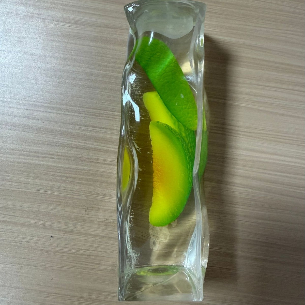 Clear squishy bar with green and yellow fruit wedges suspended inside on a desk