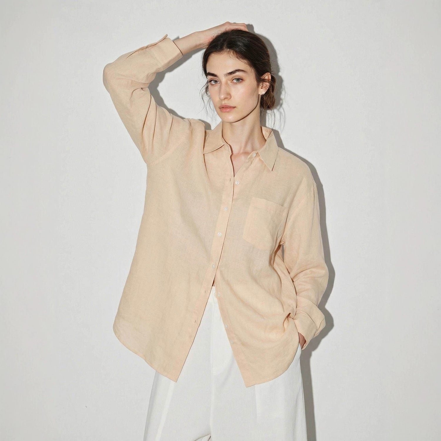 Side view of a woman in a lightweight linen blend button-up shirt with long sleeves and drop hem