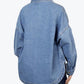 Back view of a washed blue denim shirt jacket with a yoke seam, dropped shoulders and a rounded hem with a side vent