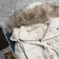 Furry hood trim and snap collar tab of the white quilted jacket seen from above on a lace cloth
