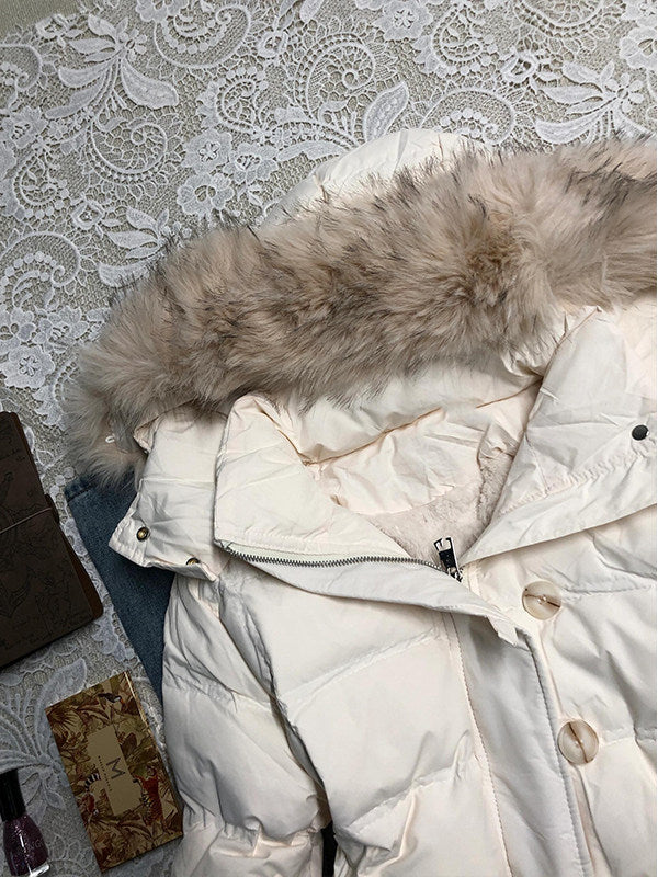 Furry hood trim and snap collar tab of the white quilted jacket seen from above on a lace cloth