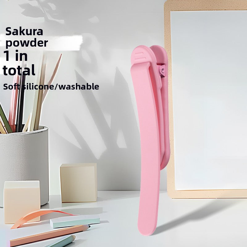 Single sakura pink silicone bookmark clip standing on a desk beside a pen cup