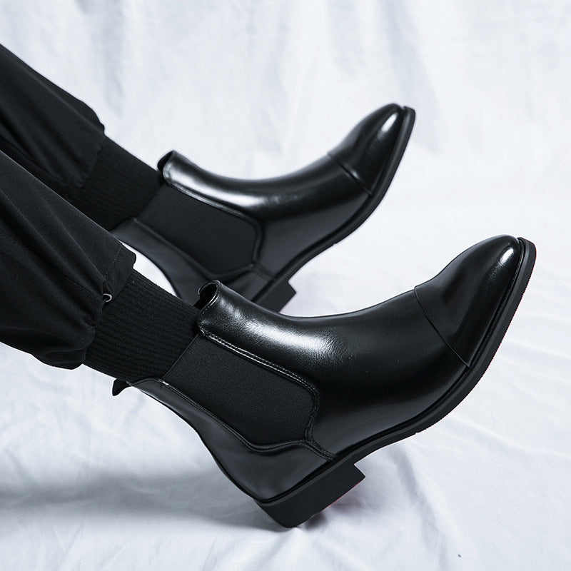 Side view of black Chelsea ankle boots with pointed cap toe, elastic gusset and low block heel on white fabric