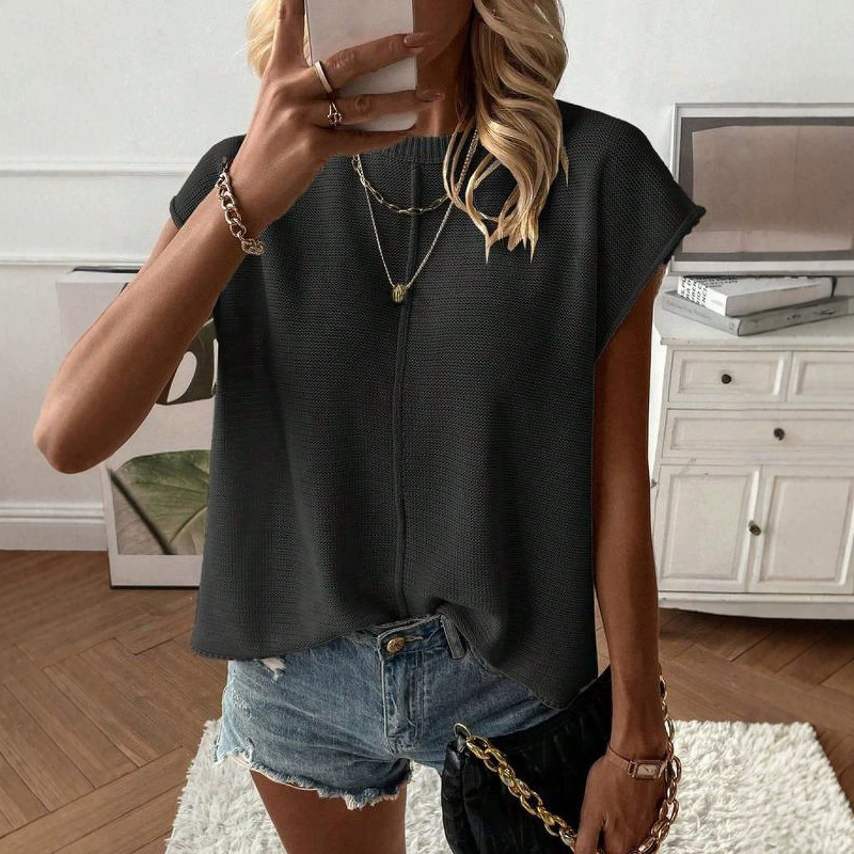 Solid color cap sleeve knit top with a round neck shown on a model against a plain room