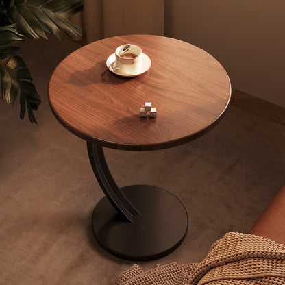 Dark walnut tone round side table seen from above with a black curved steel arm and disc base next to a sofa