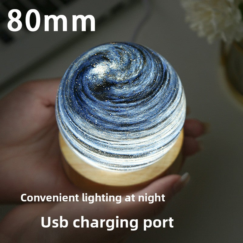 Hand holding a glowing swirl glass planet night light on a wooden base, 80mm diameter, USB charging port