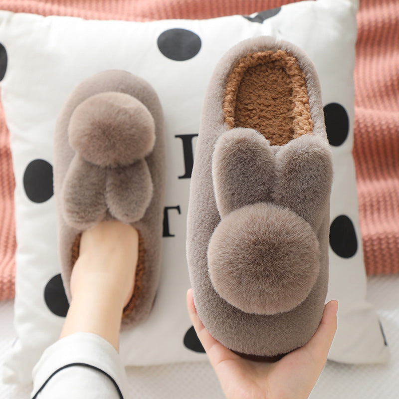 Brown plush bunny slippers pair with pom pom tails and caramel lining, one on a foot, brown variant