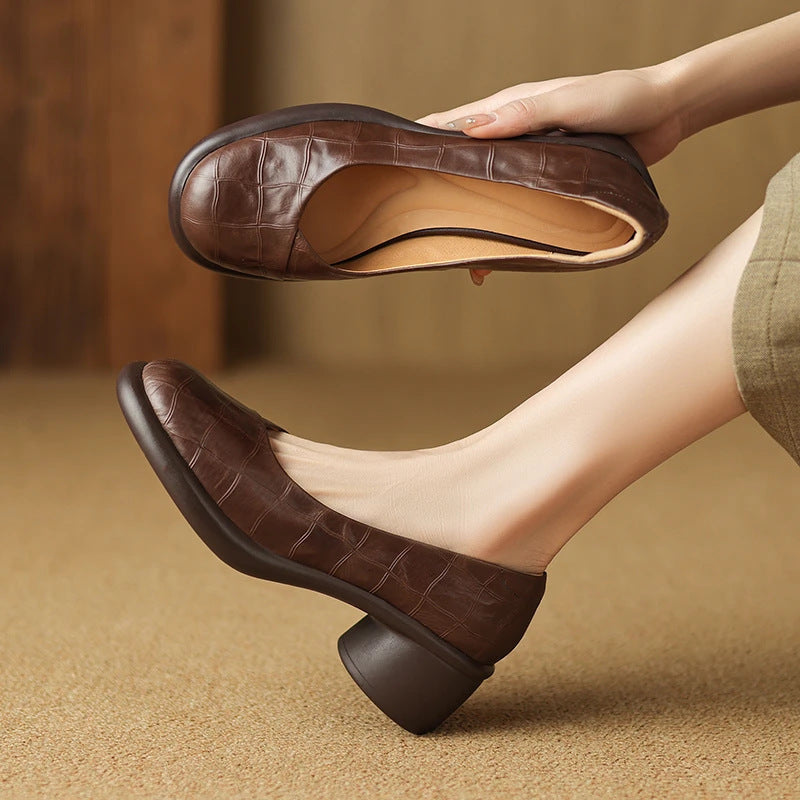 Brown embossed leather round block heel slip-on shoe worn on a foot, the other held to show the insole