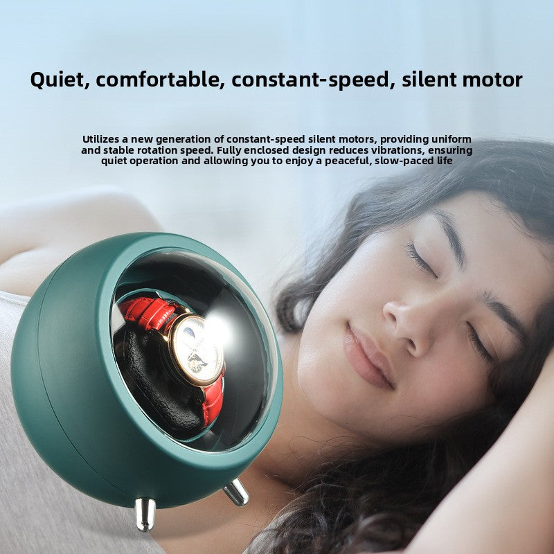 Emerald green watch winder turning a wristwatch on a nightstand beside a sleeping person