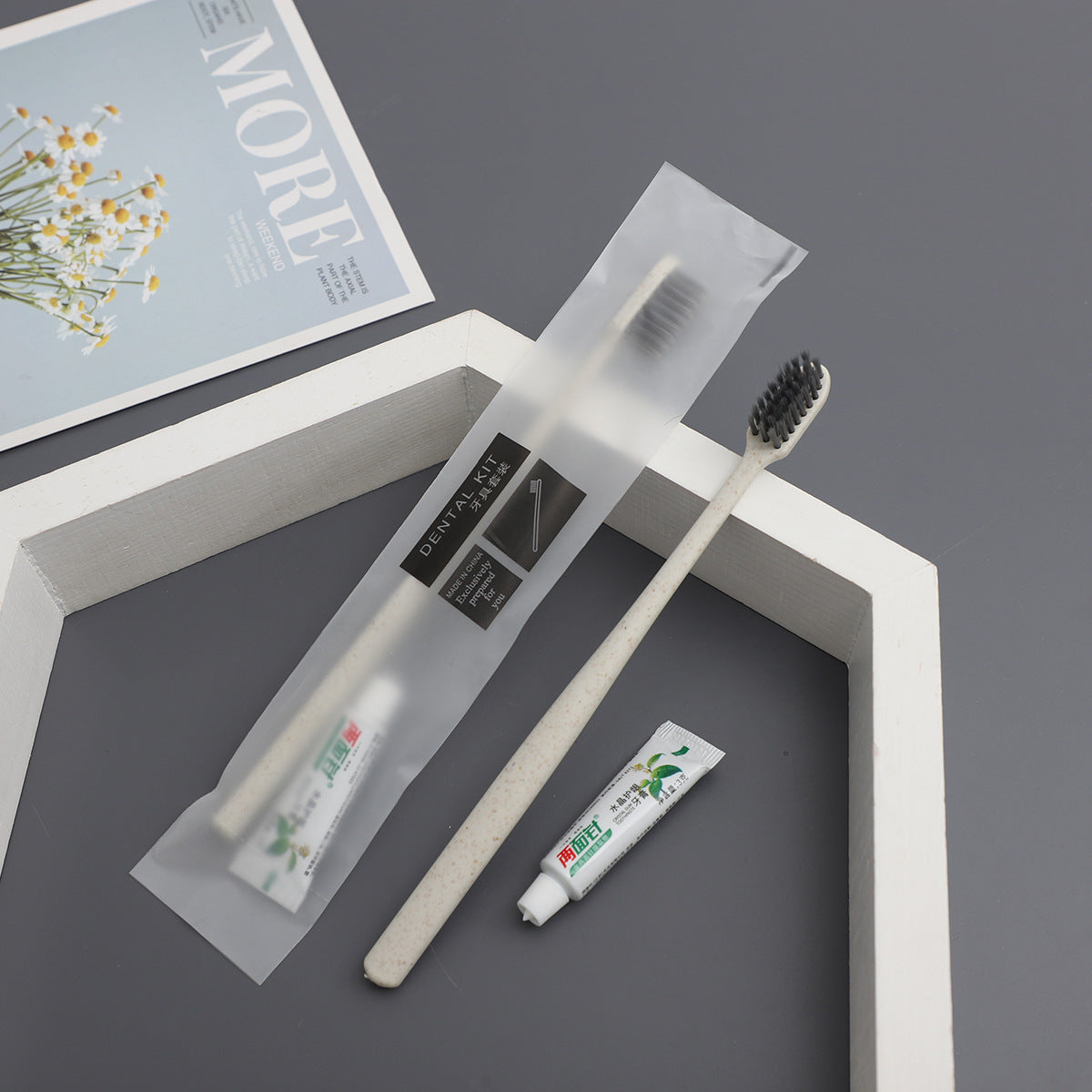 Beige straw toothbrush, toothpaste tube and a frosted dental kit pouch on a gray surface