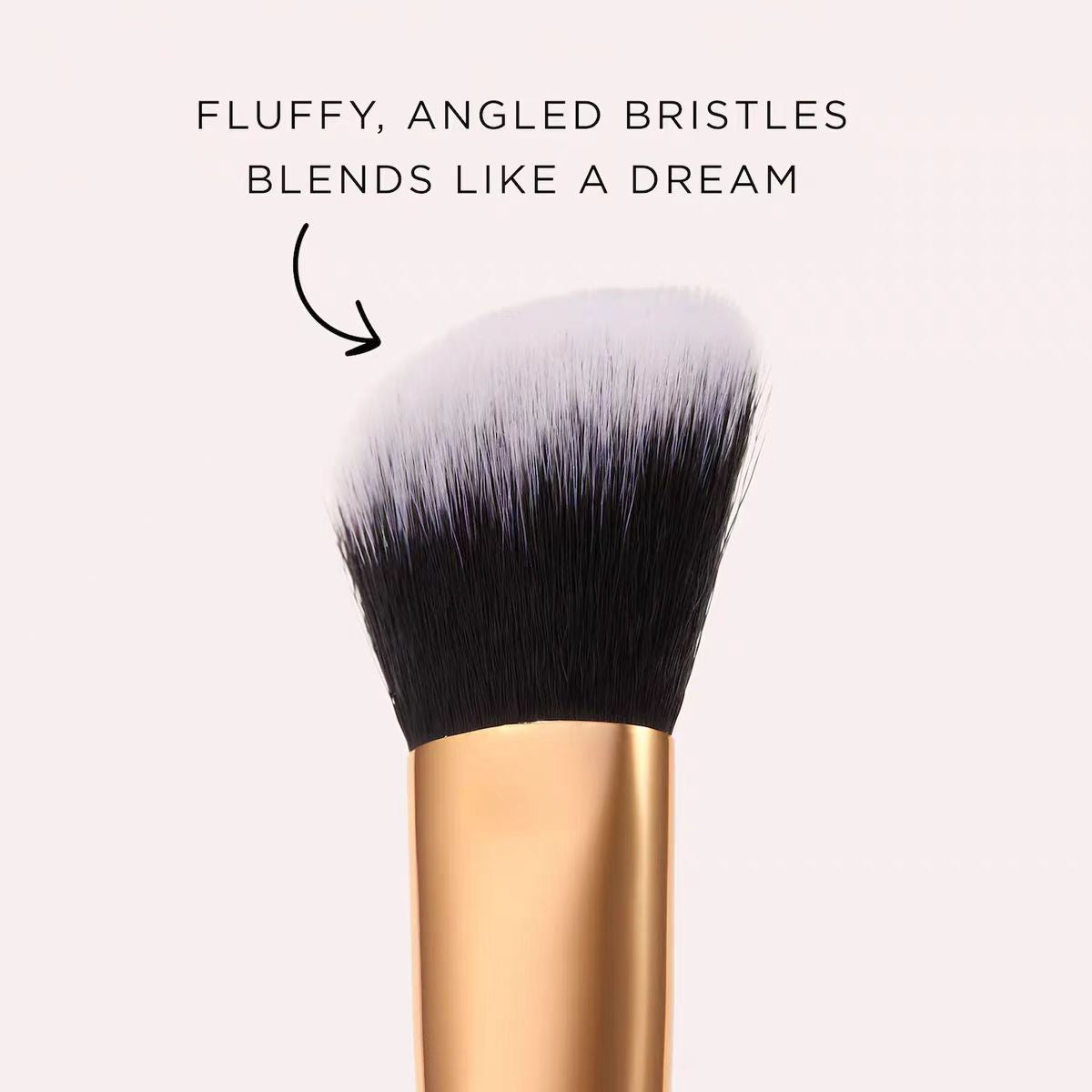 Close up of the fluffy angled two tone bristles in white and black above a gold tone ferrule on a pale pink background