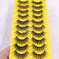 Thick fluffy cat eye false strip eyelashes in black on a yellow ten pair tray, close up on the fluffy cat eye flare