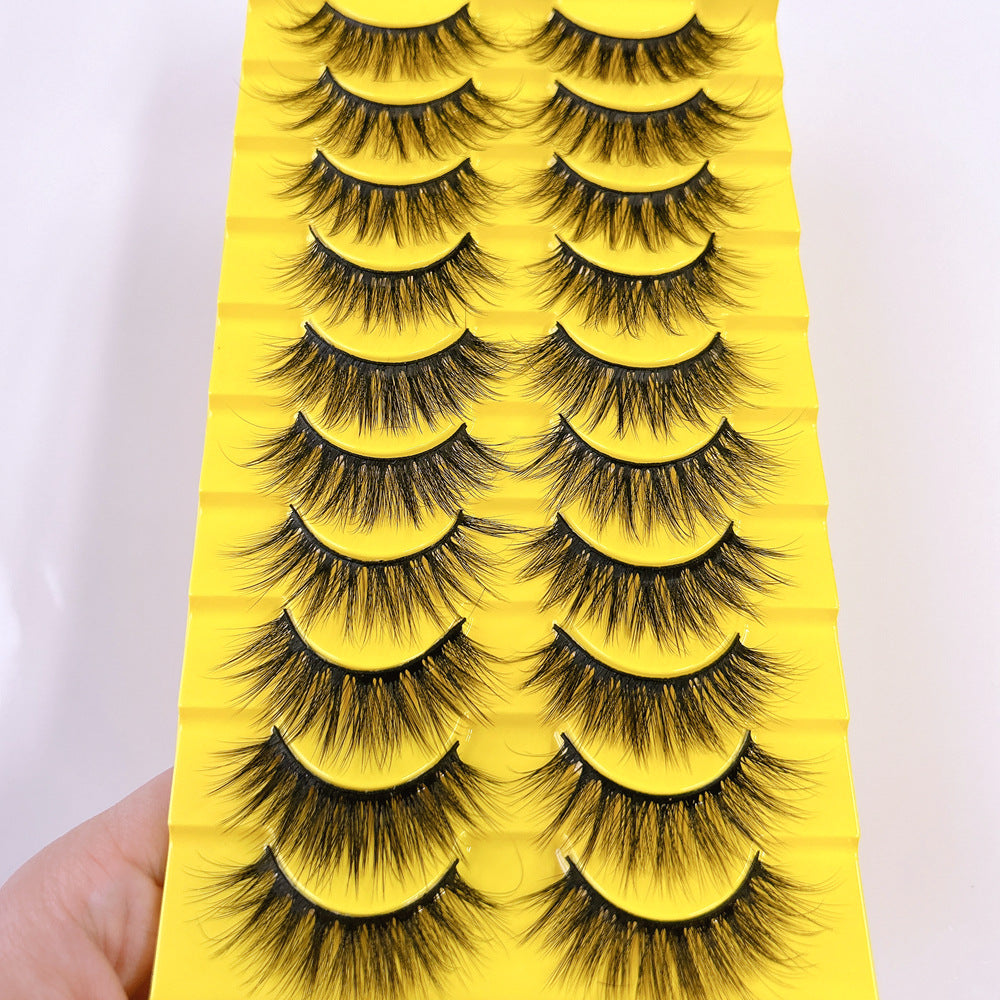 Thick fluffy cat eye false strip eyelashes in black on a yellow ten pair tray, close up on the fluffy cat eye flare