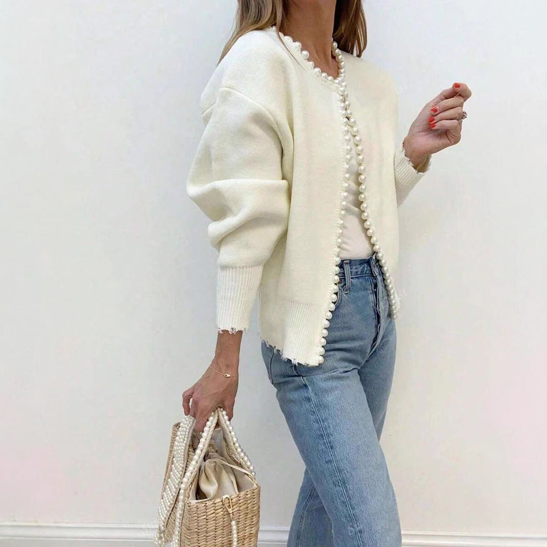 Side view of the cream faux pearl trimmed knit cardigan worn open over jeans