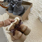 Gray ankle boots with ribbon bows in a box above a hand holding chestnut shearling cuff boots with a brown bow