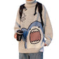 Light gray turtleneck sweater with a knitted blue shark, holding a coffee cup, on a white background