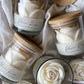 White rose candle in a glass jar with a bamboo lid, tipped on its side among linen and wooden discs