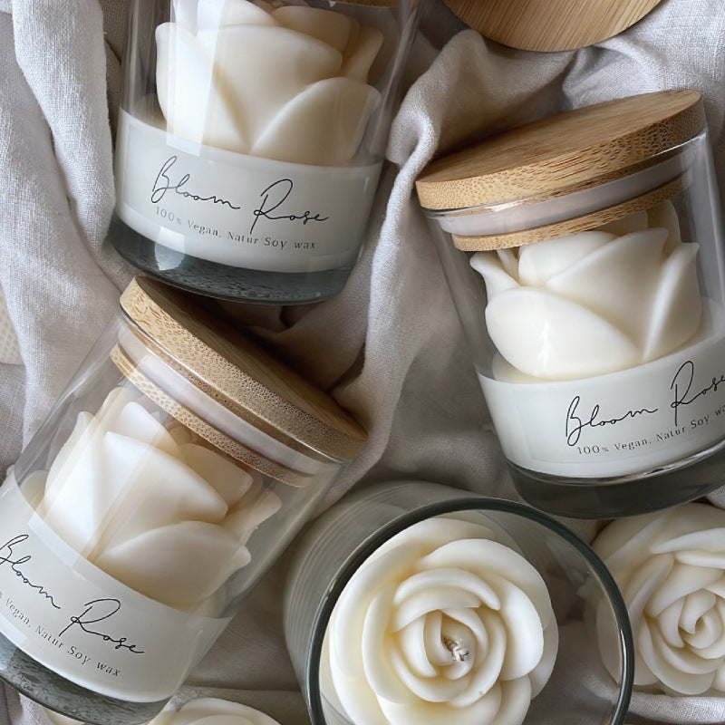 White rose candle in a glass jar with a bamboo lid, tipped on its side among linen and wooden discs
