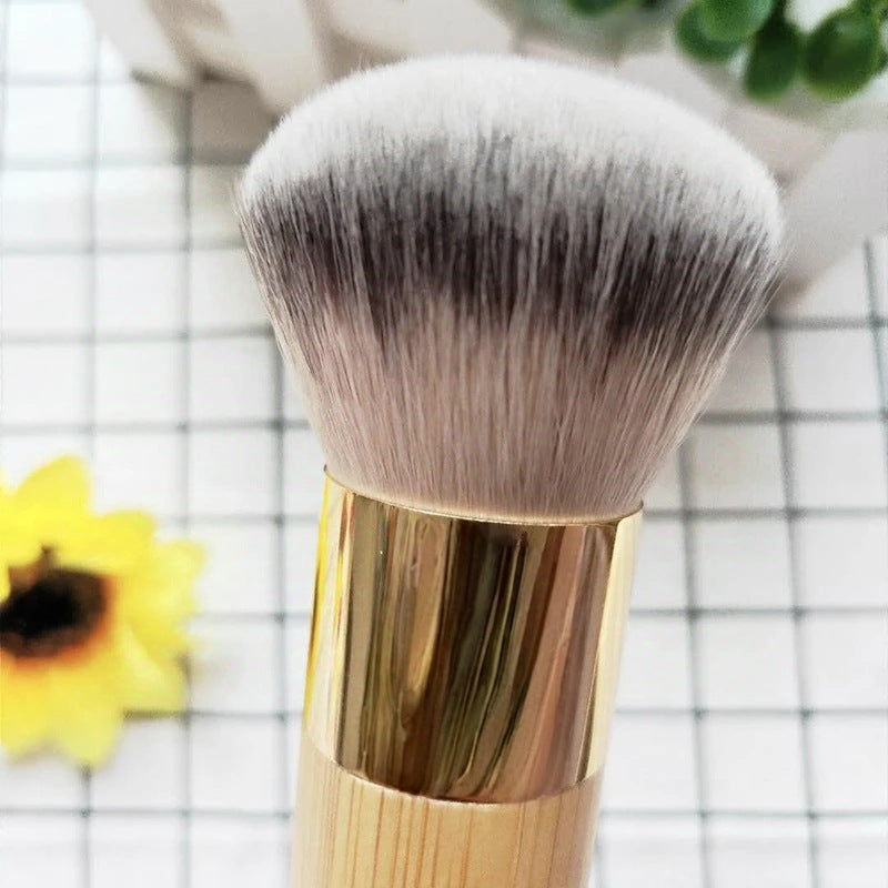 Large domed two tone bristle head above a gold tone ferrule on a bamboo handle beside a yellow flower on a checked cloth