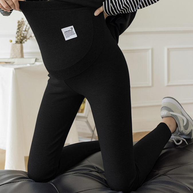 Black option photo of black maternity leggings with belly panel and label, woman kneeling on a sofa, size XXL